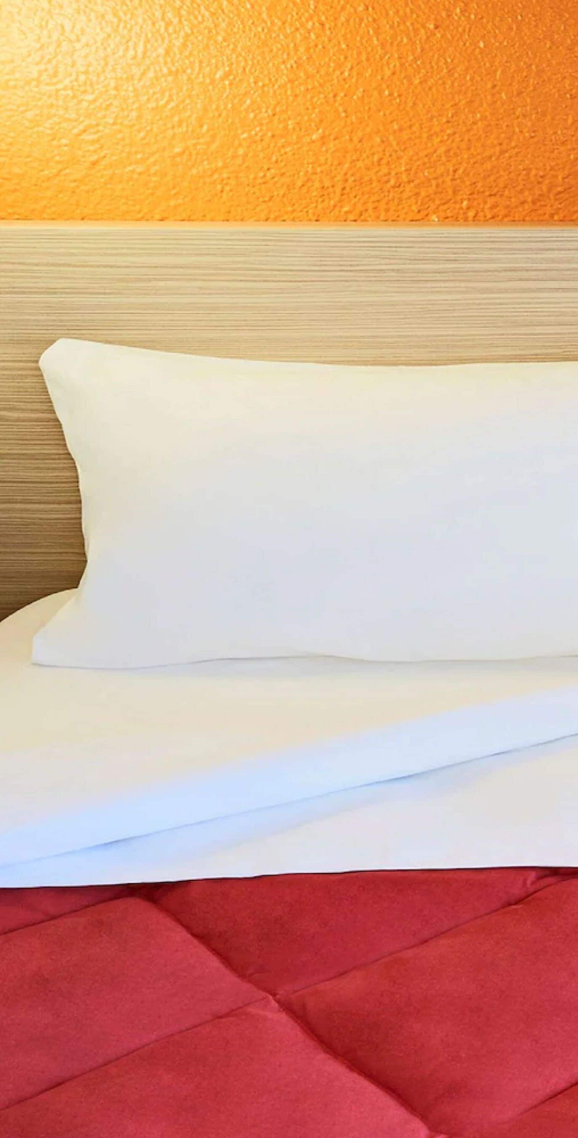 Ein ordentlich bezogenes Bett mit einem weißen Kopfkissen und einer roten Bettdecke.