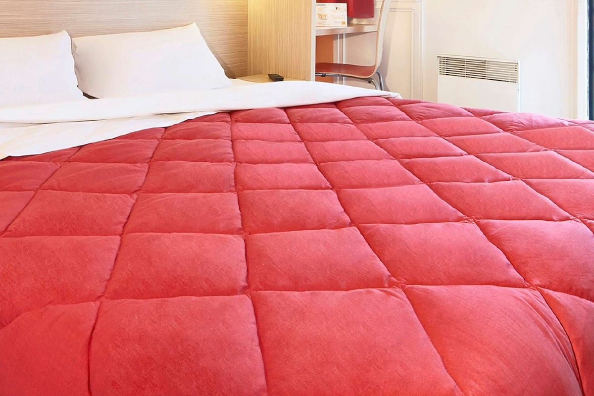 A bed with a red quilted bedspread and white pillows in a hotel room.