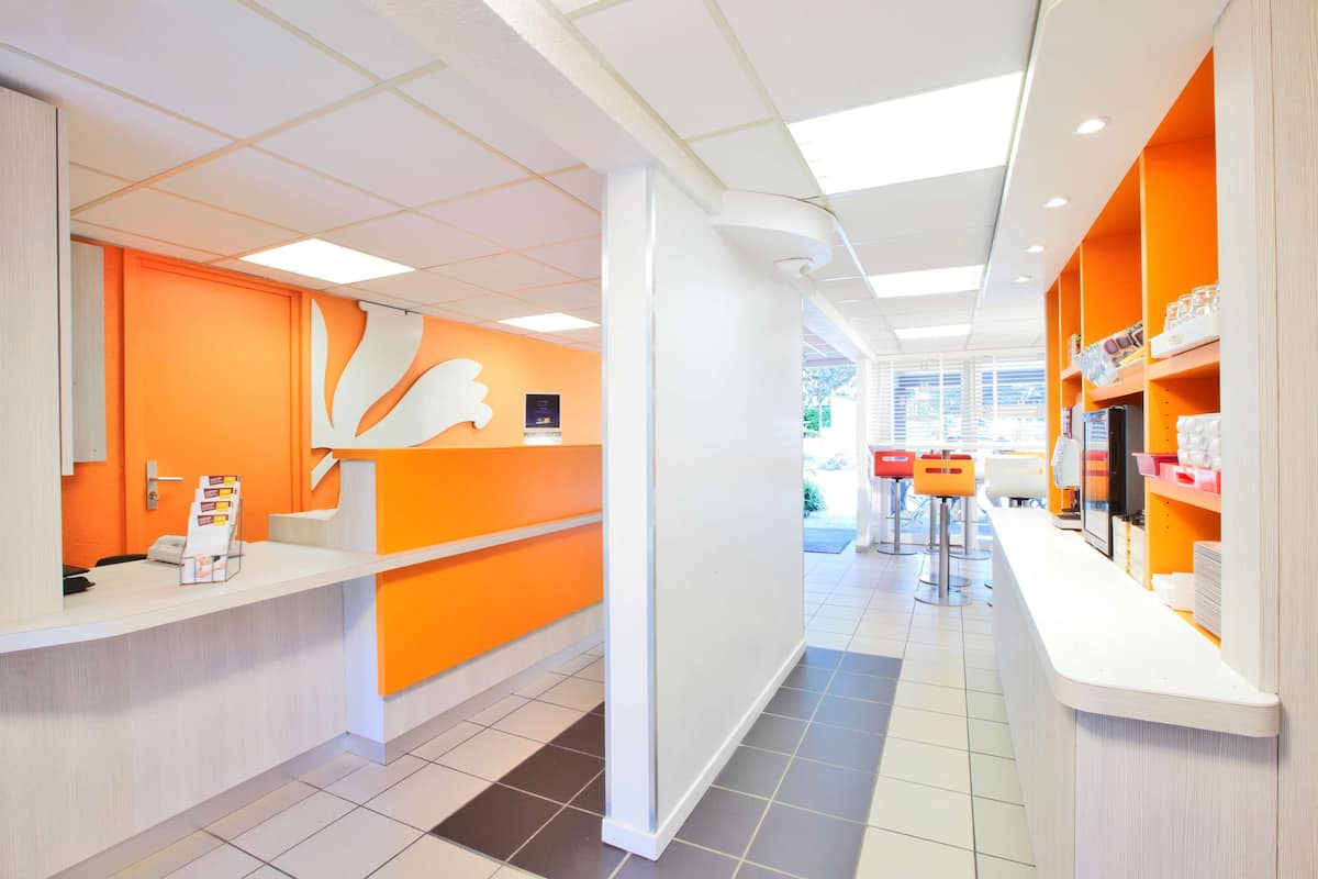 A modern reception area with a bright orange color scheme, a white reception desk, and a view of the outdoor seating area.