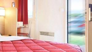 Une chambre d’hôtel avec un grand lit, un bureau, une chaise et une vue sur l’extérieur, accessible par une porte-fenêtre coulissante.
