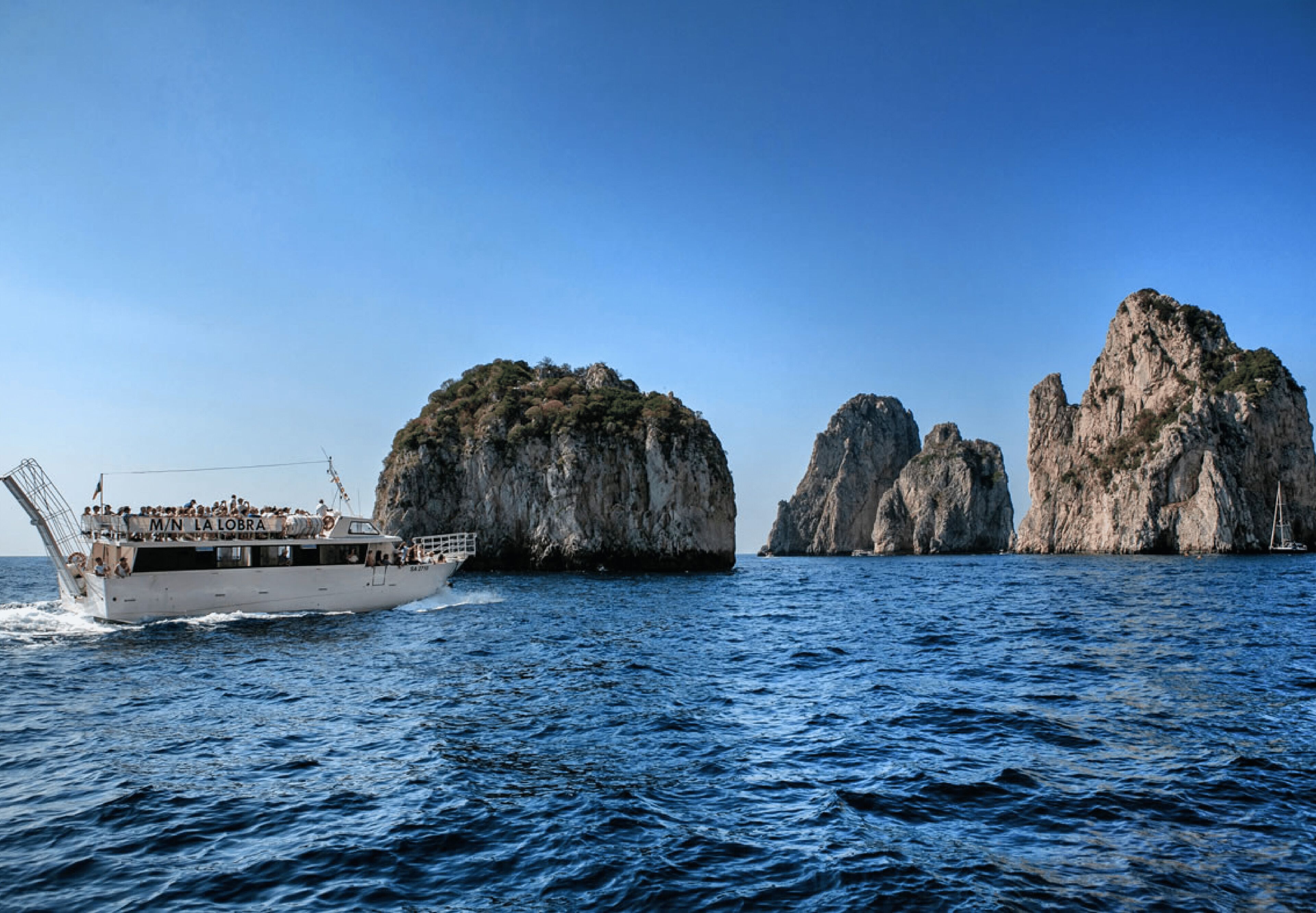 A boat with passengers, rocky formations, and calm sea.