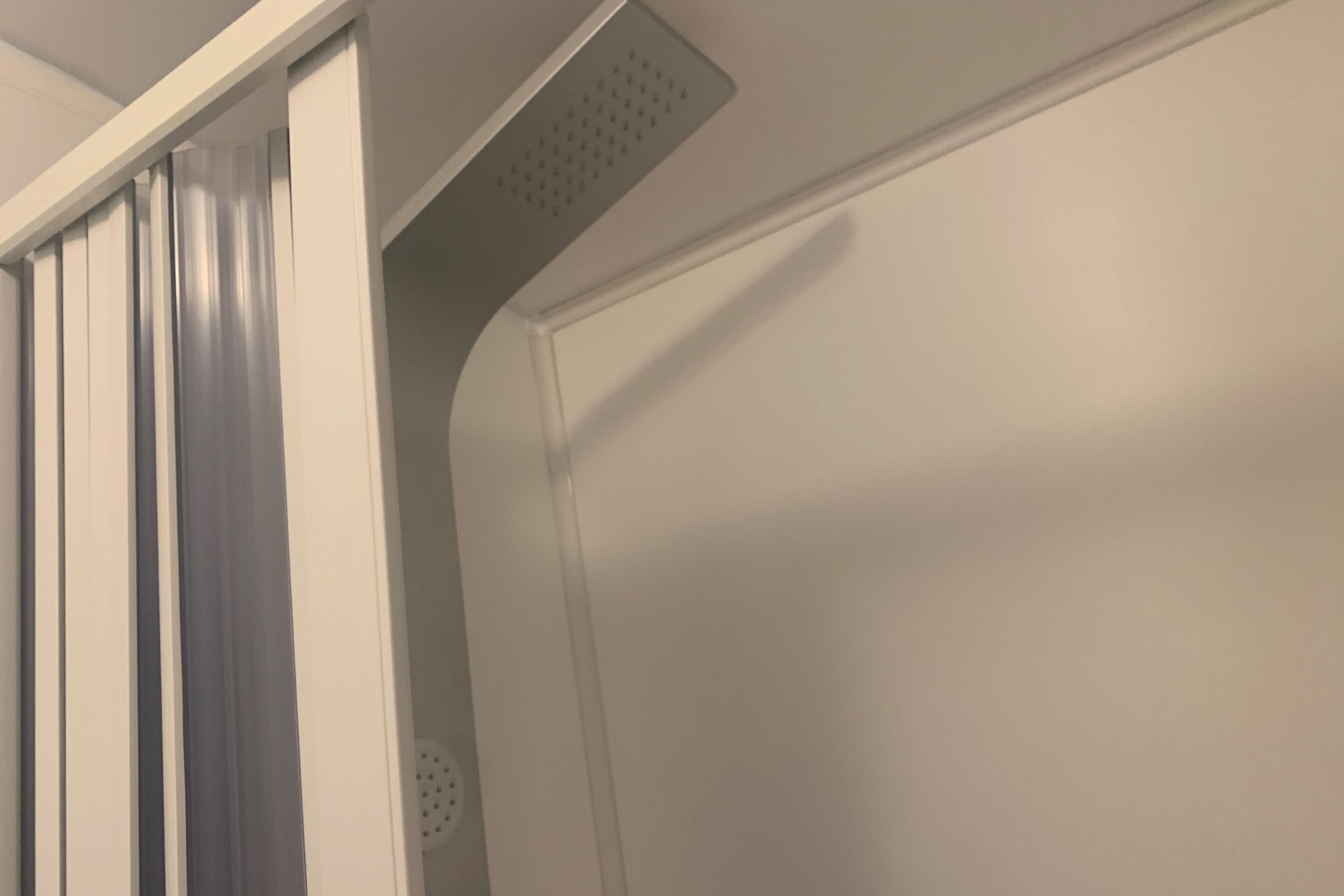 Une salle de bain avec un espace douche, une porte blanche et une bouche d’aération au plafond.