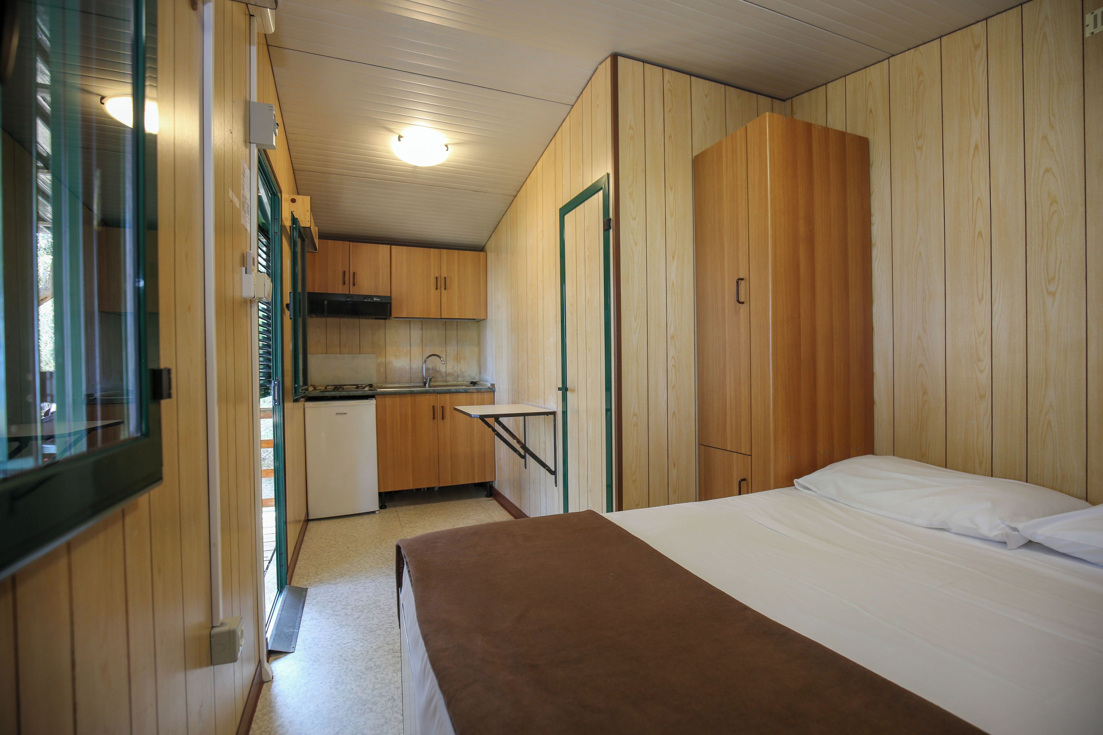 A compact room with a bed, a small kitchenette, and wooden walls.