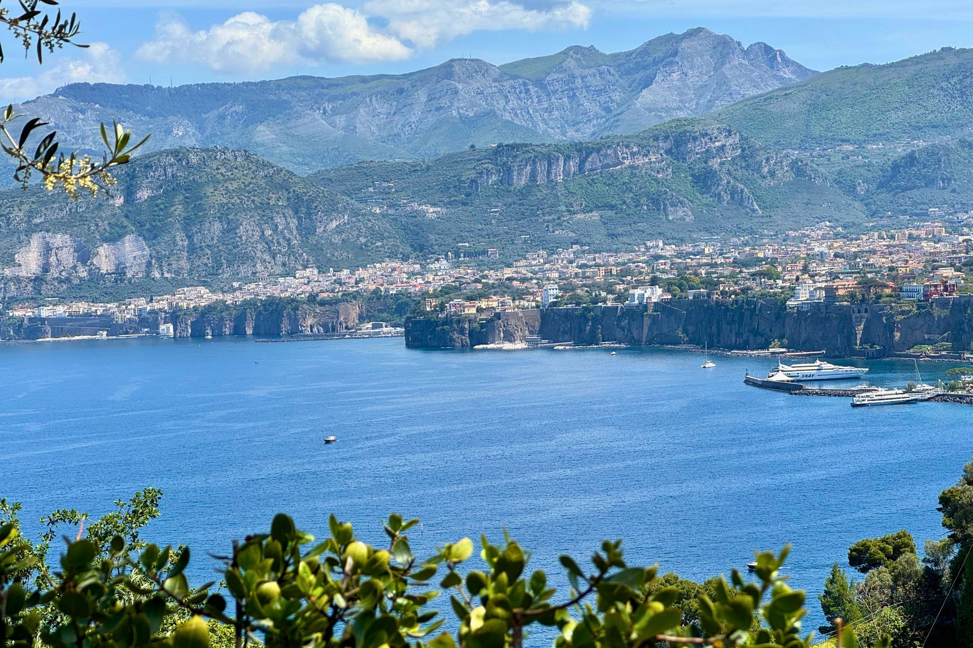 Un paysage urbain côtier avec un port, des montagnes en arrière-plan et une mer bleue et limpide.