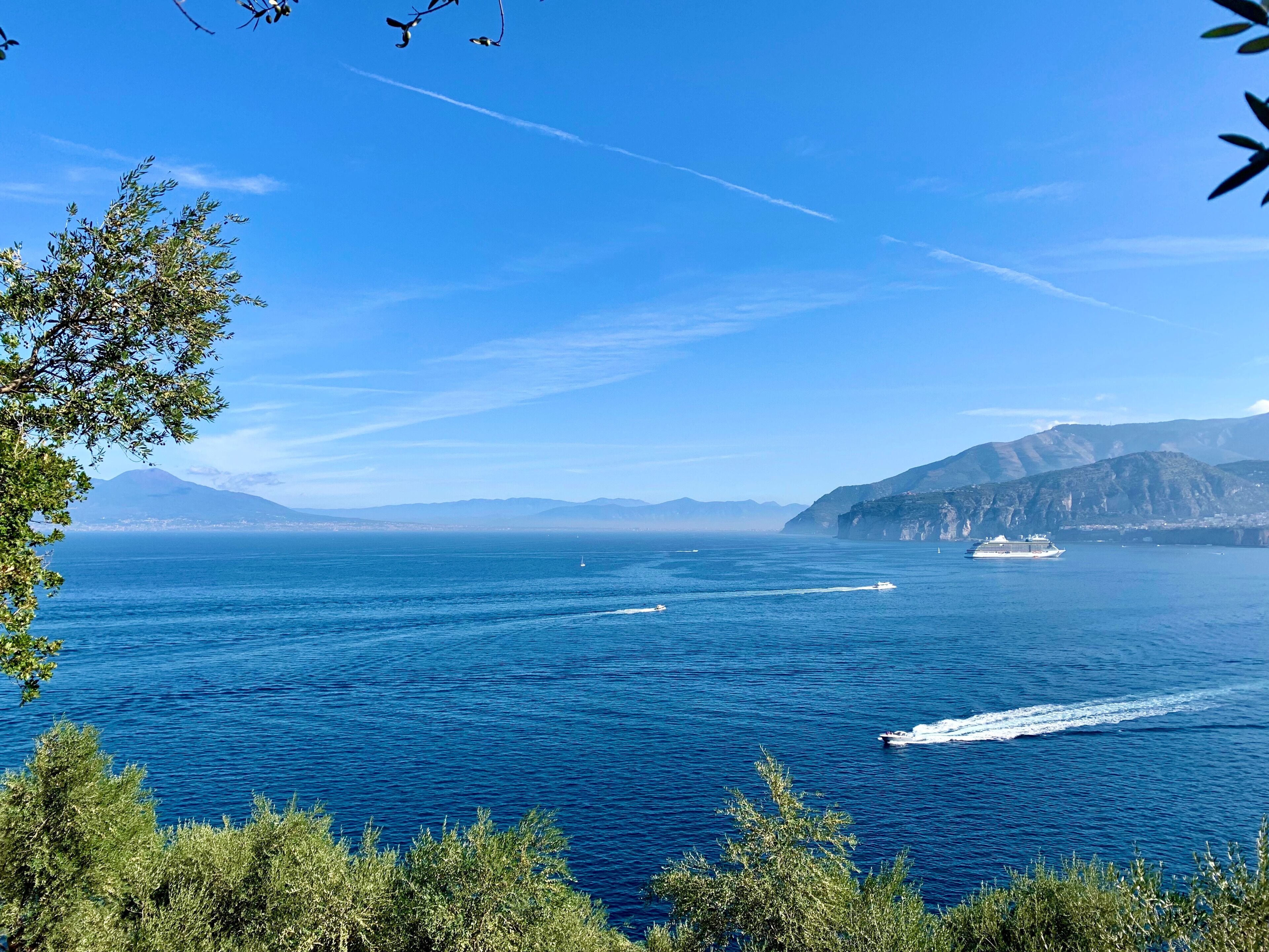 A coastal view with a cruise ship, clear blue sea, and distant mountains.