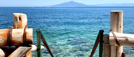 Un muelle de madera se extiende sobre aguas azules cristalinas, con una montaña al fondo.