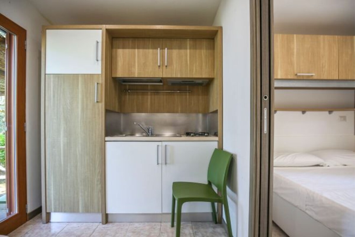 A compact room with a kitchenette, a single bed, and a green chair.