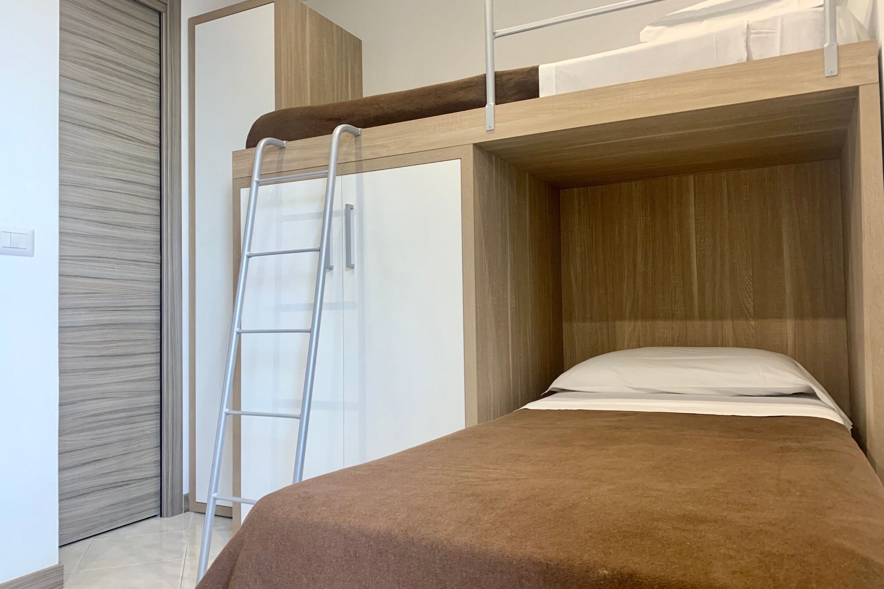 Un lit superposé avec une échelle, une porte blanche et une tête de lit en bois.
