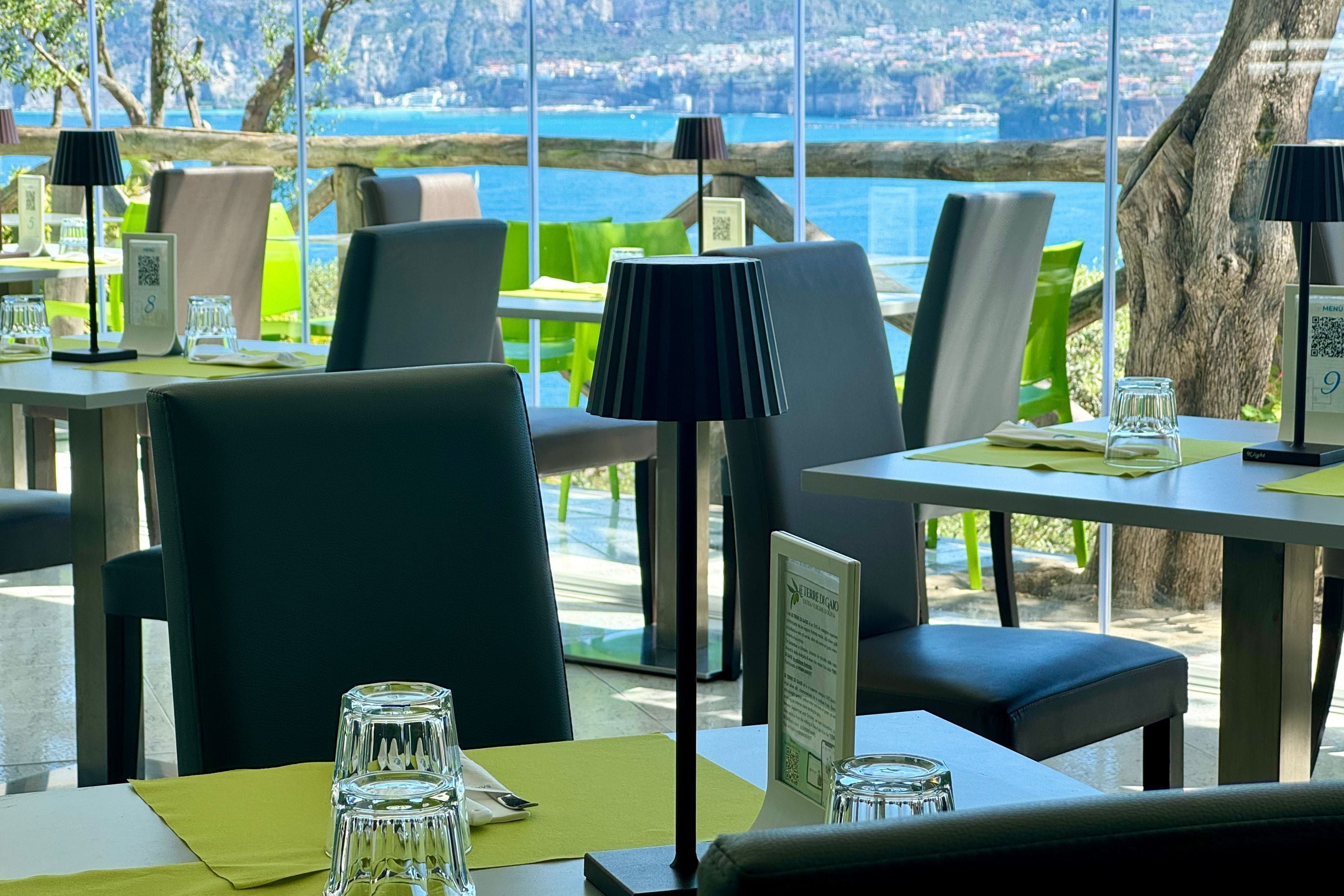 A restaurant with tables and chairs, a view of the sea, and a menu stand.