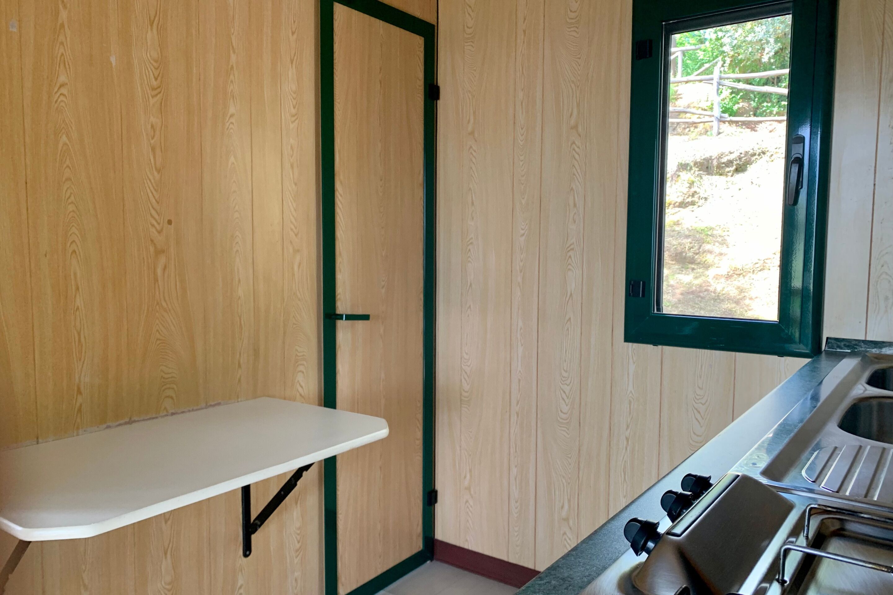 Cocina compacta con encimera blanca, pileta y ventana.