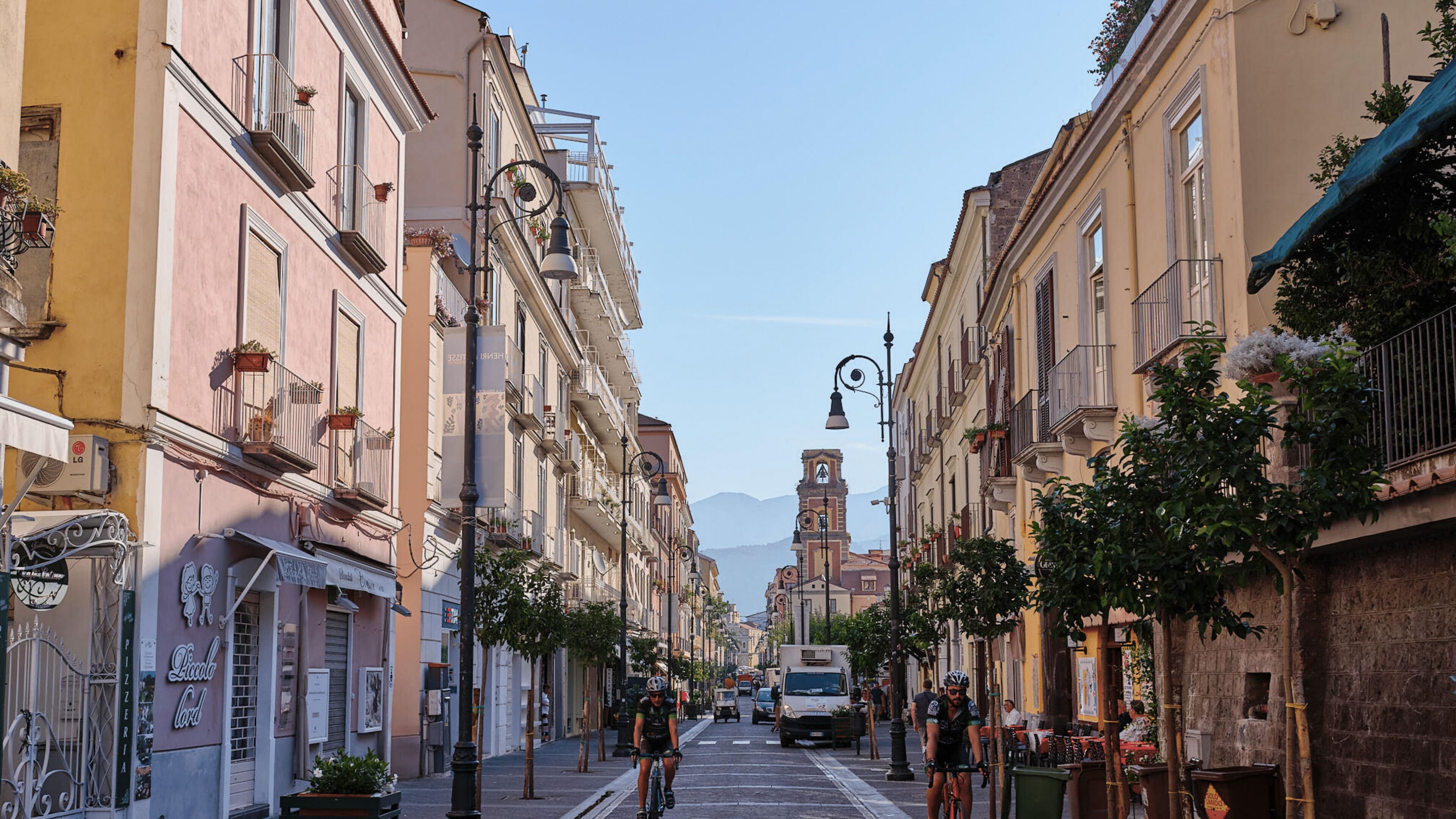 A narrow street lined with historic buildings, a bell tower, and a cyclist.