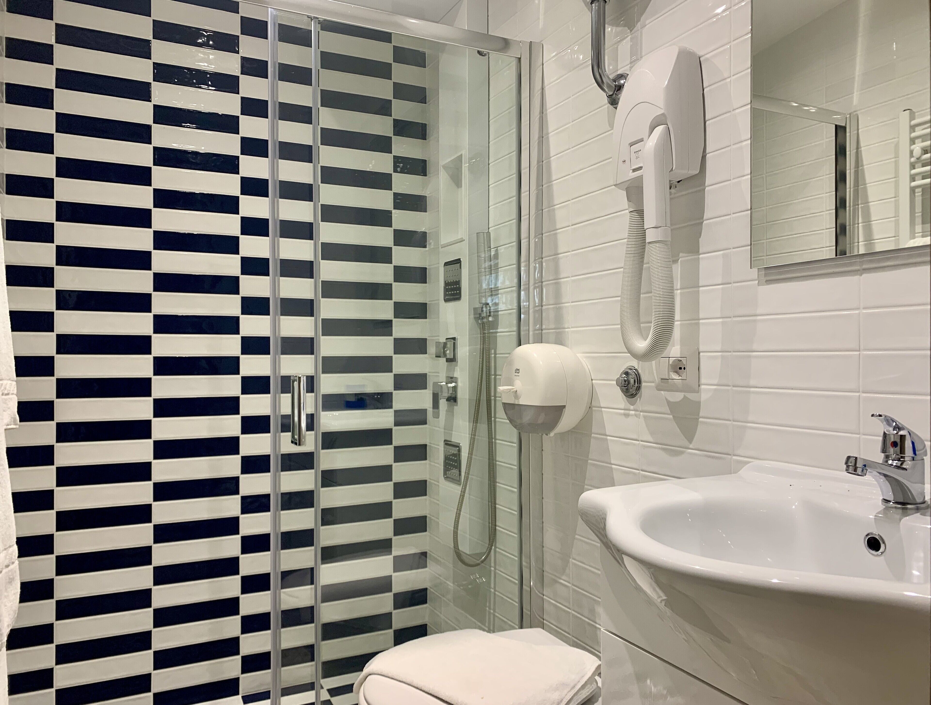 Un baño con ducha de mampara de vidrio, un lavabo blanco y un perchero para toallas.