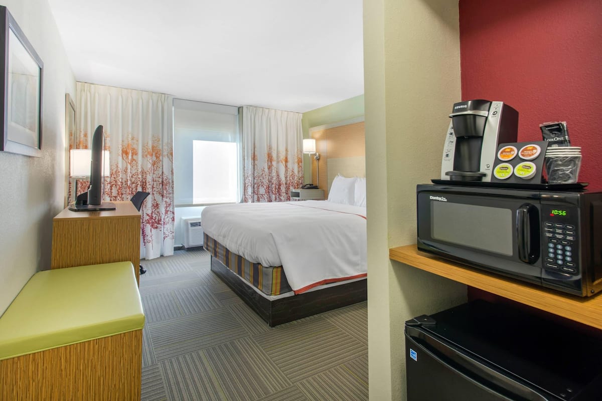 A hotel room with a bed, a desk, a microwave, and a refrigerator.