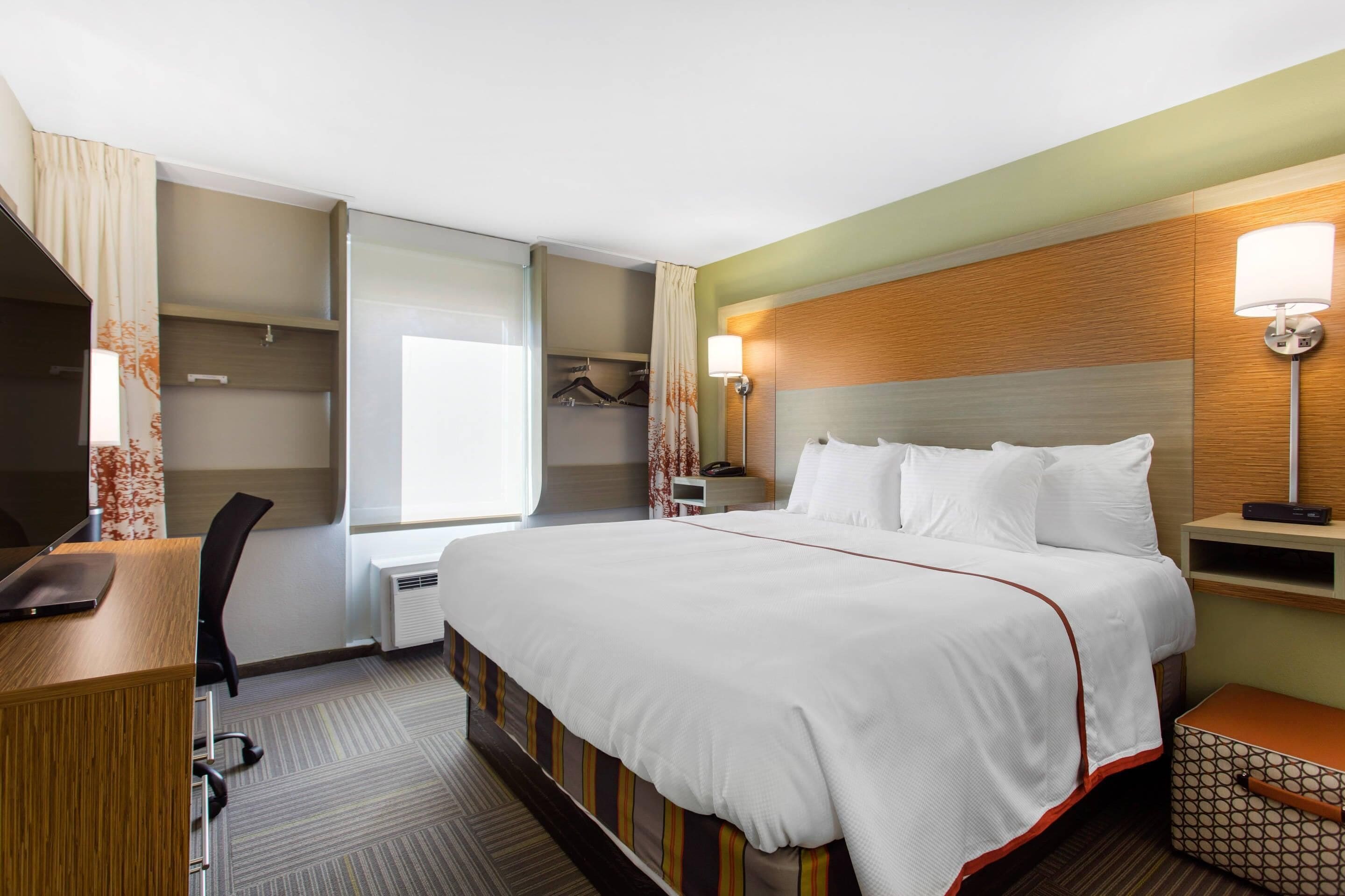 Een hotelkamer met een groot bed, een bureau, een stoel, een kledingkast en een raam met gordijnen.