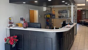 A reception desk with a black counter, a glass partition, and a view of the city through the glass. There are chairs, a small plant, and a bulletin board with notices. - Gallus Stadium Park Inn, an Ascend Collection Hotel (Columbia)