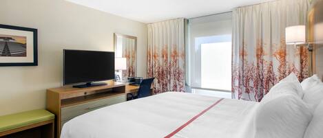 Une chambre d’hôtel avec un lit, un bureau avec une télévision, une chaise et une fenêtre avec des rideaux.