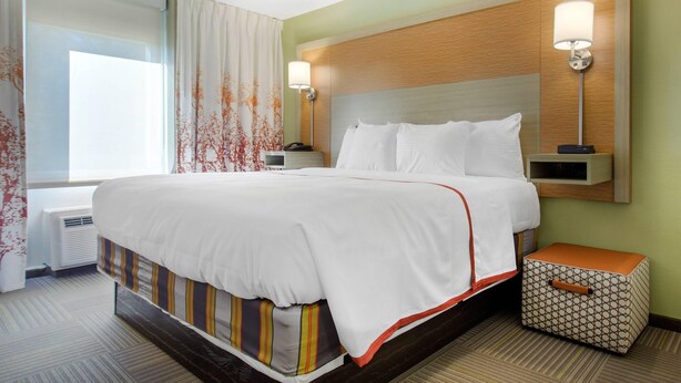A hotel room with a large bed, two bedside tables, a nightstand, a wall-mounted lamp, and a window with curtains. - Gallus Stadium Park Inn, an Ascend Collection Hotel (Columbia)