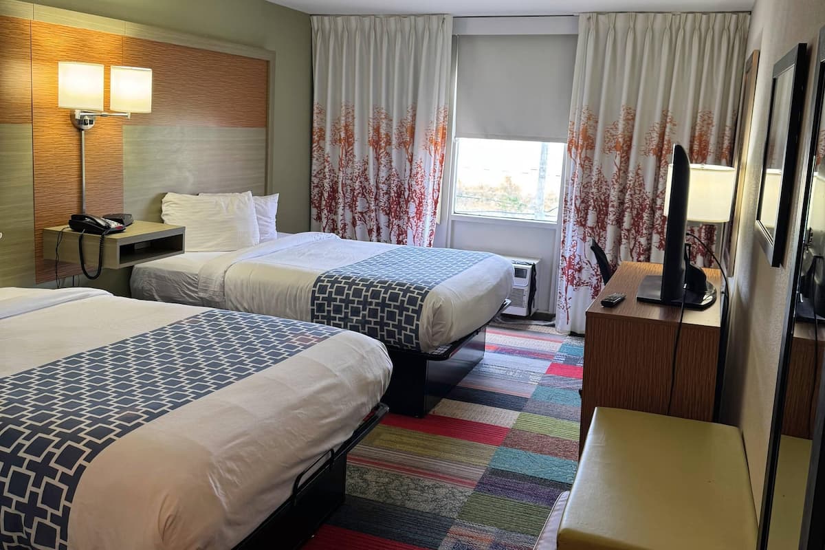 A hotel room with two beds, a desk with a lamp, a telephone, and a television.