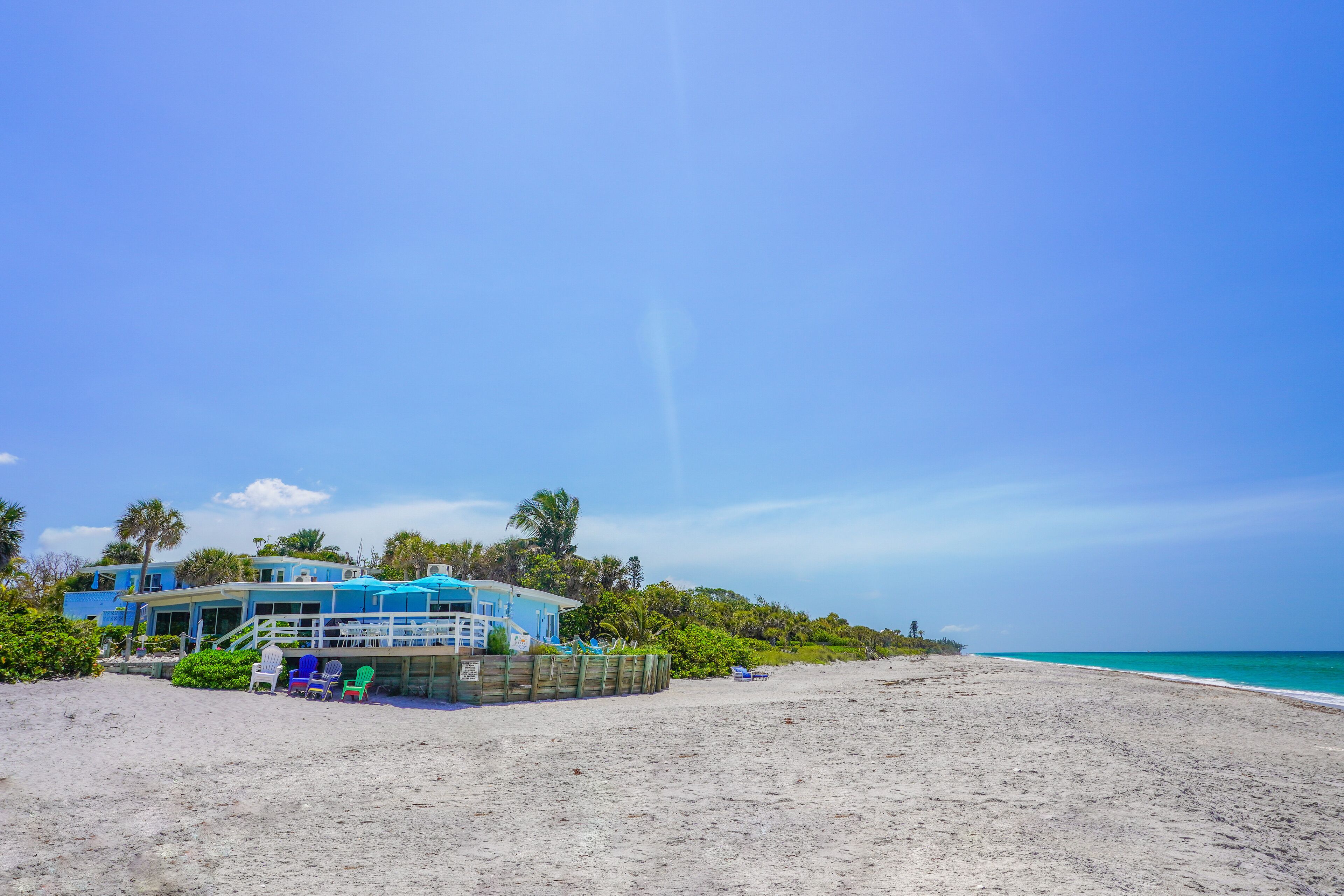 A beachfront property with a large house, a covered patio, and a sandy beach.
