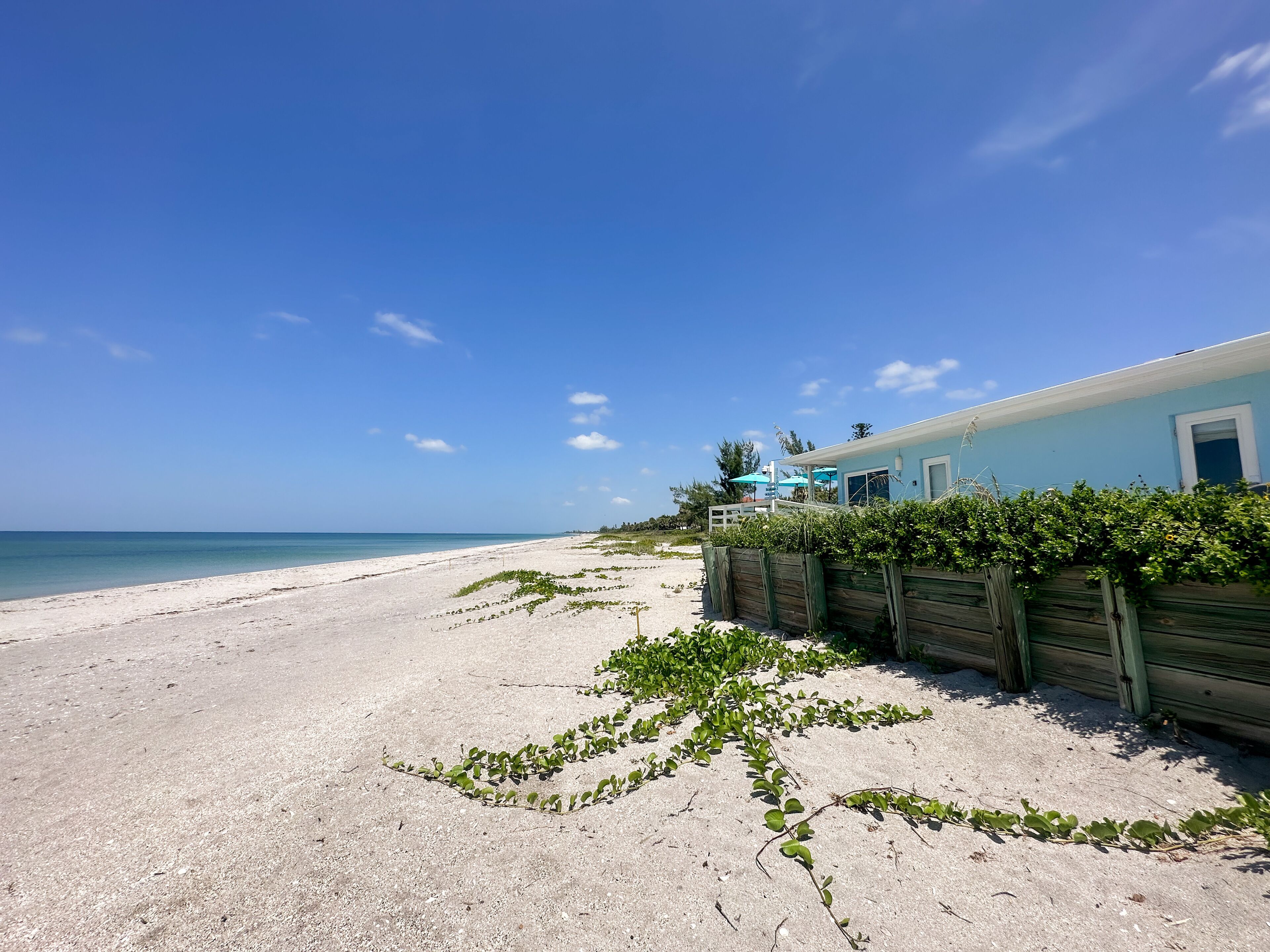 A beach view with a house, clear sky, and calm sea.