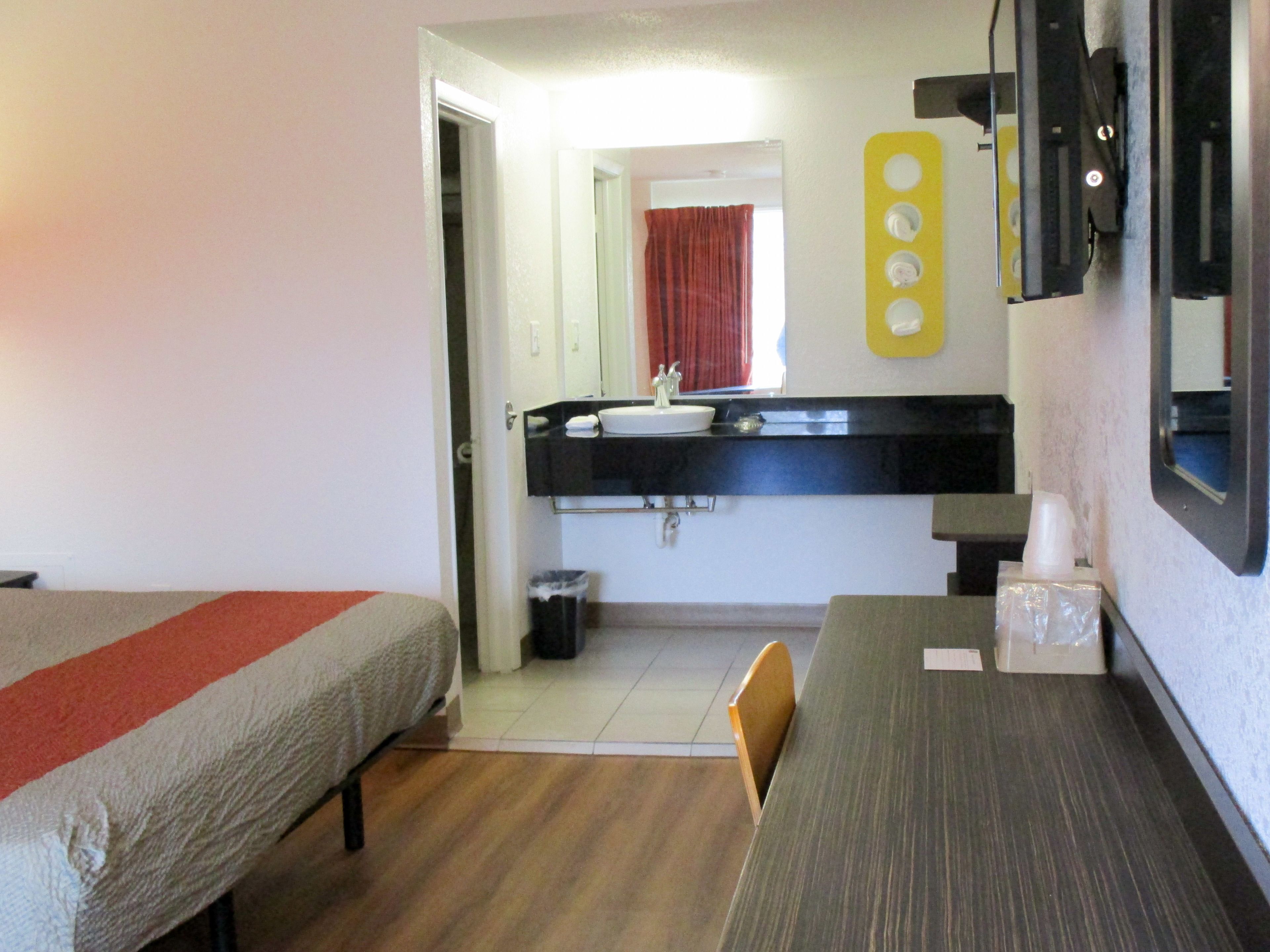A hotel room with two single beds, a small table, a sink, and a mirror.