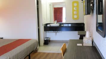 A hotel room with two single beds, a small table, a sink, and a mirror.