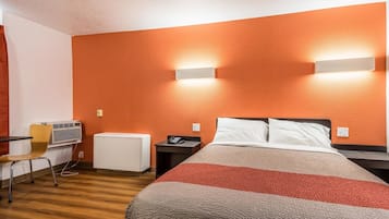 Quarto de hotel com cama, mesas de cabeceira, uma cadeira, aparelho de ar condicionado e duas luminárias fixadas na parede.