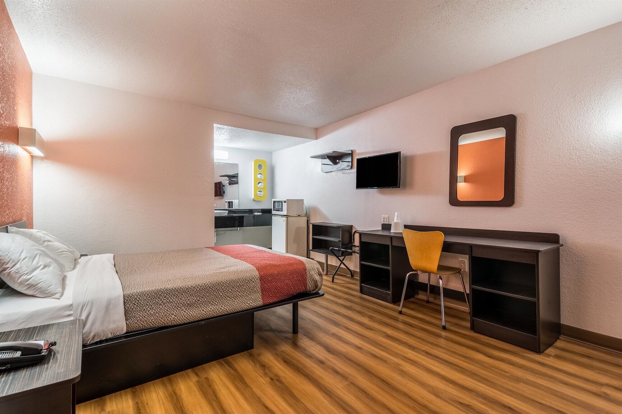 A compact hotel room with a bed, a desk, a chair, a television, and a mirror.