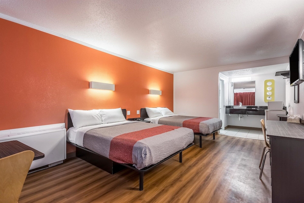 Une chambre d’hôtel avec deux lits, un bureau, un miroir et une télévision.
