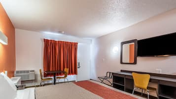 A hotel room with a bed, a desk, a chair, a television, and a window with curtains.