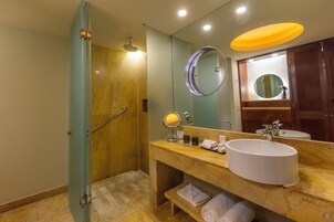 A bathroom with a shower, a sink, a mirror, and a vanity with towels.