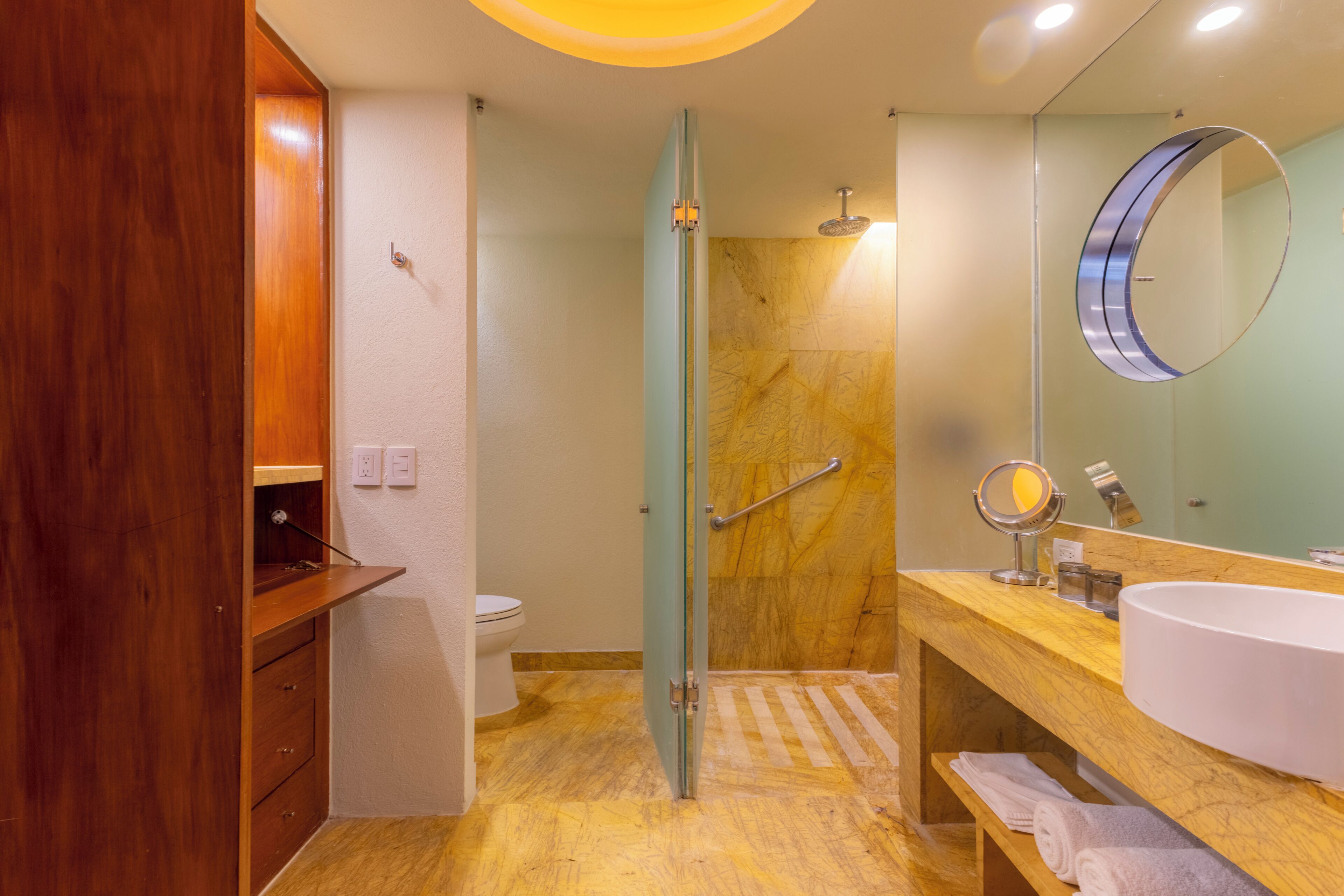 Un baño moderno con tocador de madera, un espejo grande, cabina de ducha de vidrio y lavabo blanco.