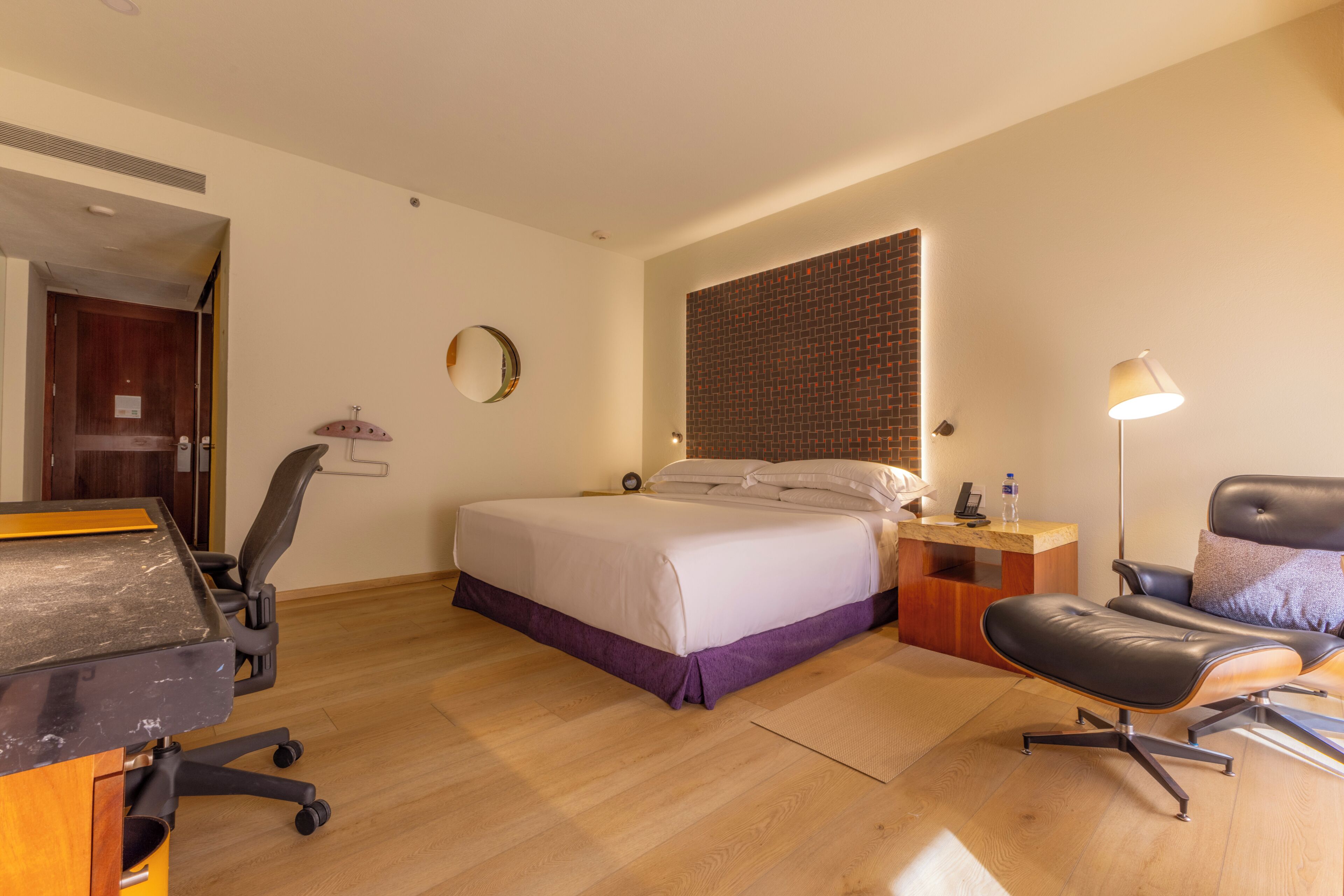 Habitación de hotel con cama, escritorio, silla y una pequeña mesa con lámpara.