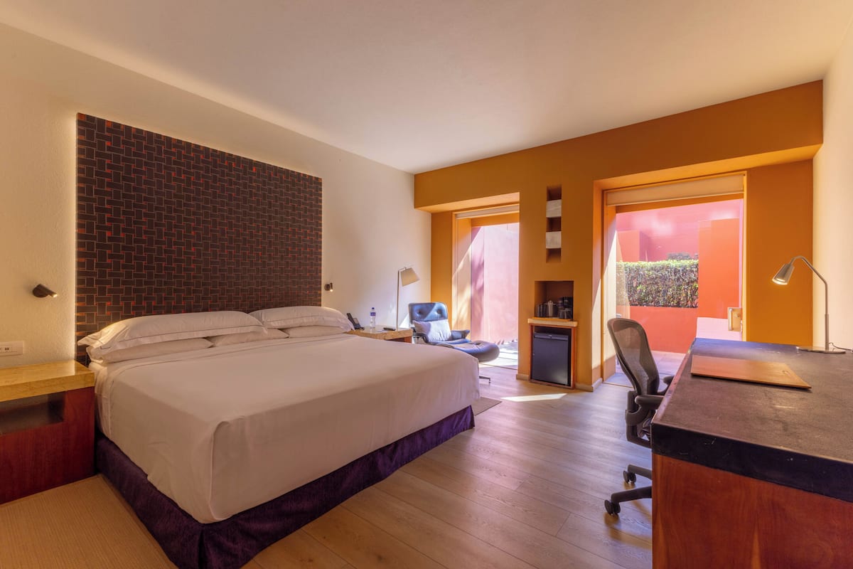 A hotel room with a bed, desk, chair, and a small kitchenette.