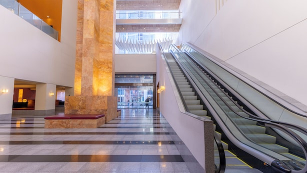 A spacious lobby with a central column, escalators, and a checkered floor pattern. - Barceló Monterrey Valle (San Pedro Garza García)
