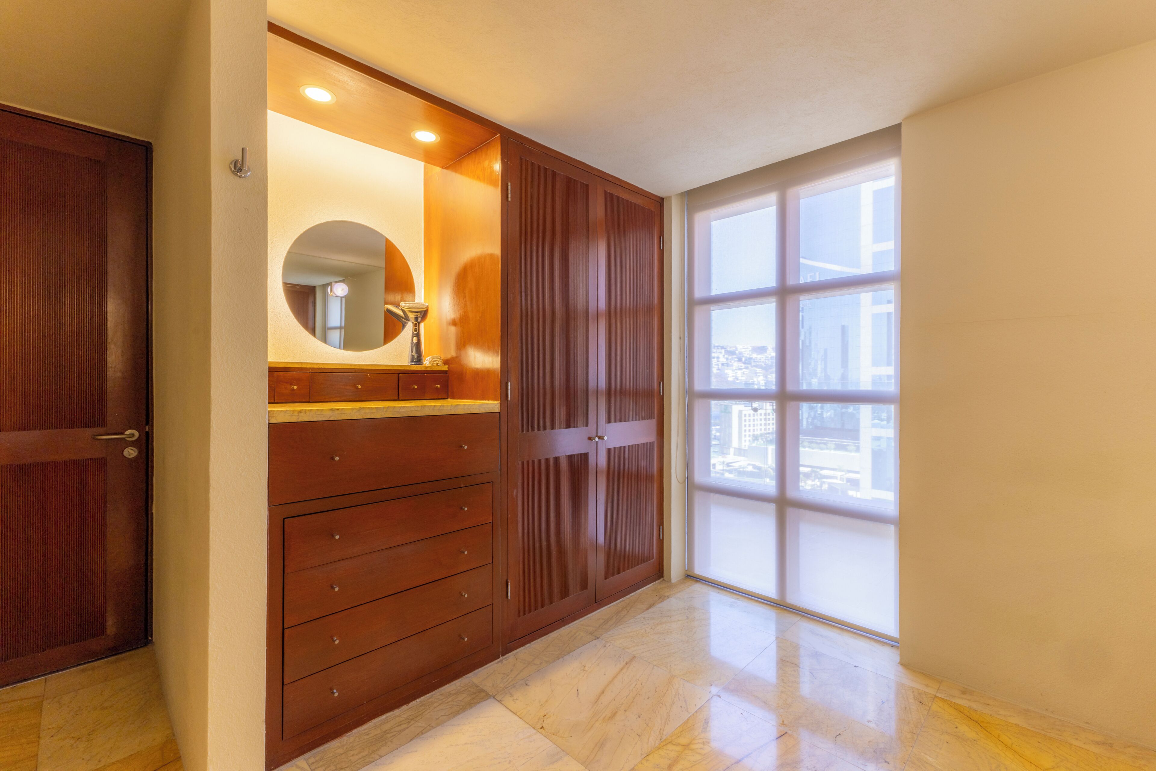 Una habitació amb un finestral gran, un armari de fusta, un mirall i una porta.