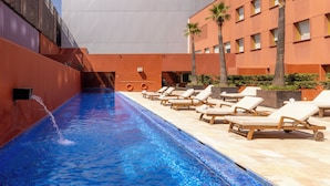 A swimming pool with lounge chairs, a water feature, and a modern building with balconies. - Barceló Monterrey Valle (San Pedro Garza García)