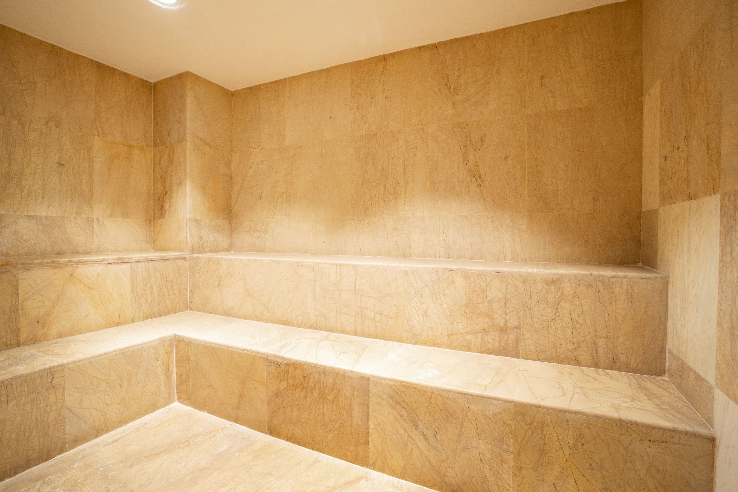 Un baño con suelo y paredes de mármol, que incluye un banco integrado y una zona de ducha.