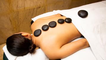 A person receiving a massage with black stones placed on their back.