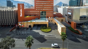A modern building with a central courtyard, surrounded by other structures, and a clear sky with clouds. - Barceló Monterrey Valle (San Pedro Garza García)