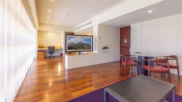 Een moderne woonkamer met houten vloer, een flatscreen televisie aan de muur, een eettafel met stoelen en een klein bijzettafeltje.