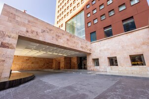 Un edificio moderno con una entrada amplia y abierta, un espacio cubierto con techo curvo y un patio con plataforma circular.