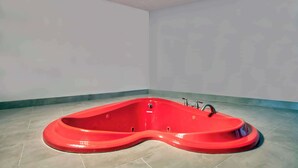 A red jacuzzi tub in a corner of a room with plain walls and tiled flooring.