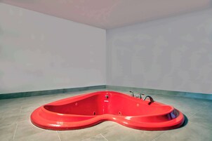Una bañera de hidromasaje roja ubicada en un rincón de una habitación con paredes lisas y suelo de baldosas.