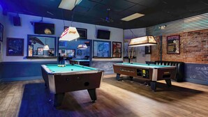 A pool table room with two pool tables, a brick wall with graffiti, and a ceiling fan.