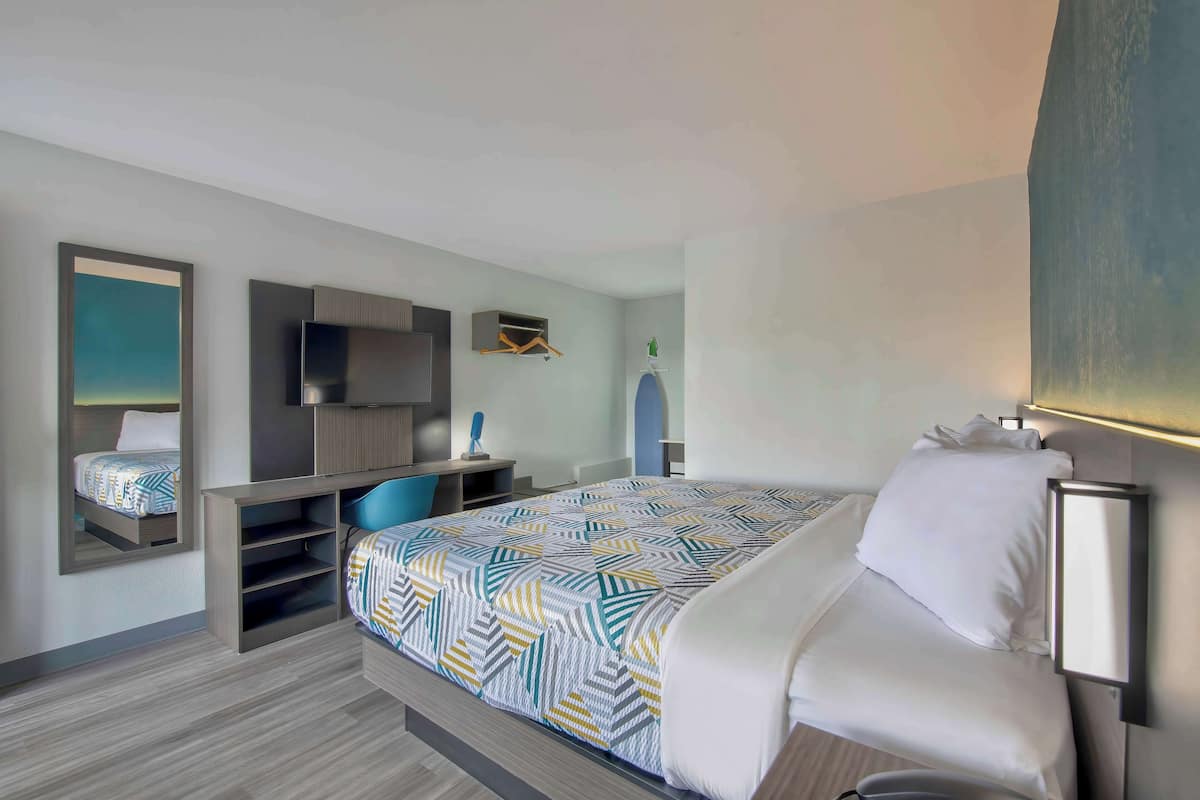 A modern hotel room with a bed, a TV, a desk, and a chair.