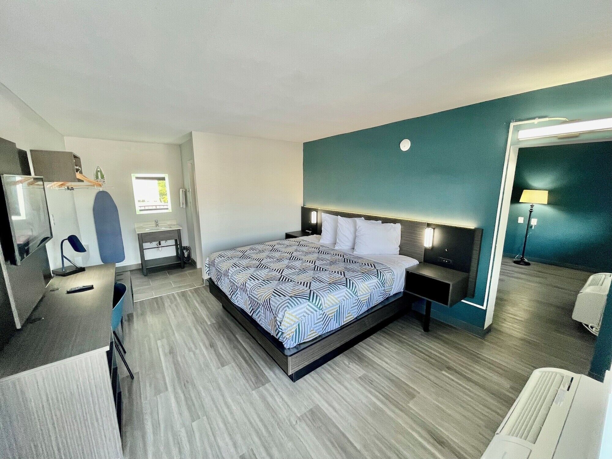 A modern hotel room with a large bed, bedside tables, a desk, and a mirror.