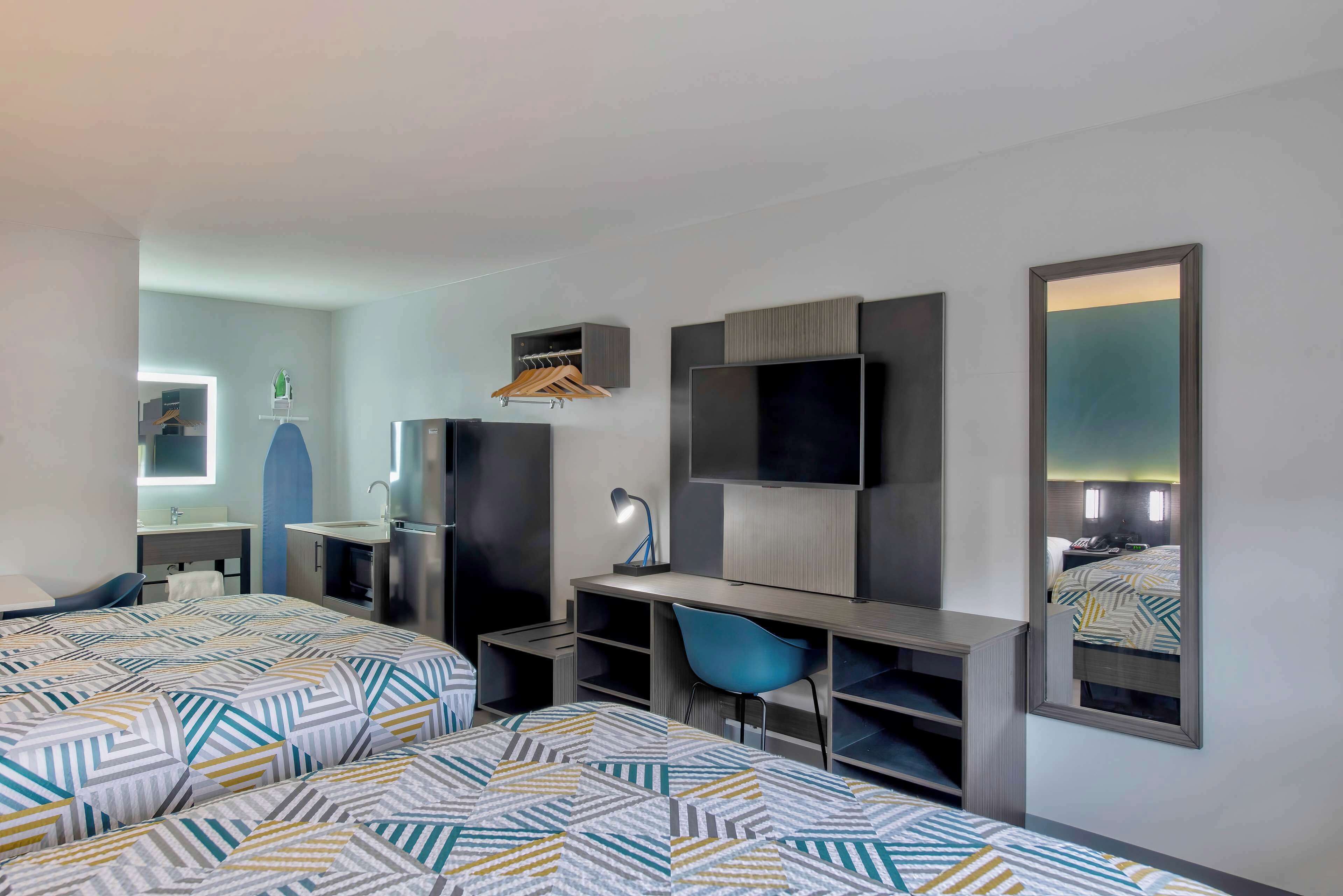 Una habitación de hotel con dos camas, un escritorio, una silla, un televisor, un espejo y un armario.