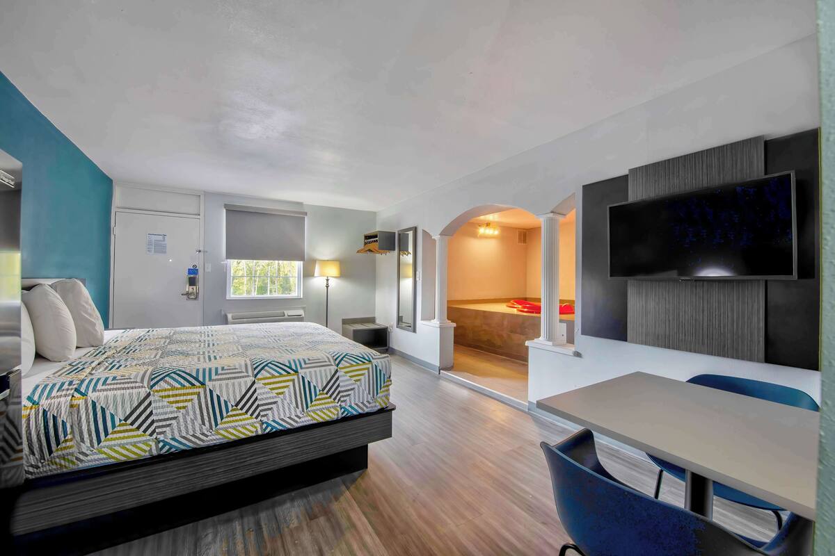 A modern hotel room with a large bed, a desk, and a TV.