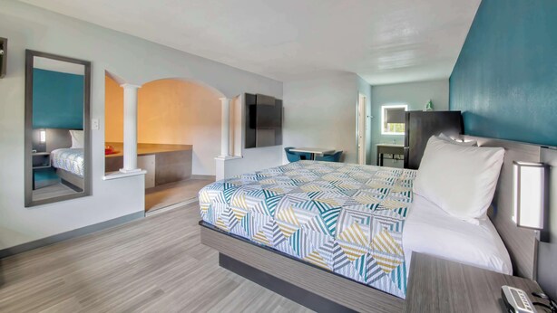 A modern hotel room with a large bed, a desk, a chair, and a TV.